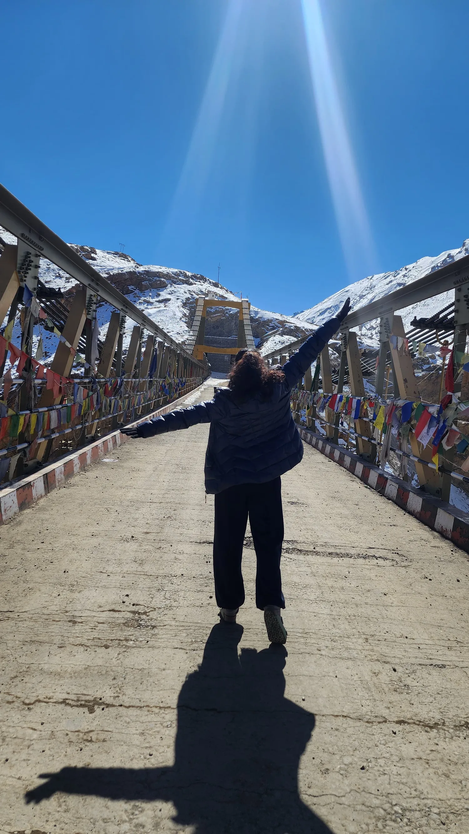 A figure on a snowy bridge, back turned, arms flung wide toward the light.