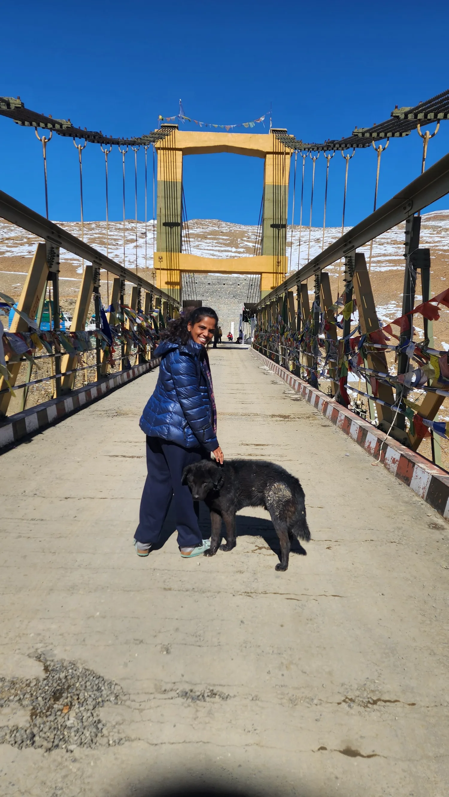 Laughing on a bridge hung with prayer flags, one hand resting on a stray dog.