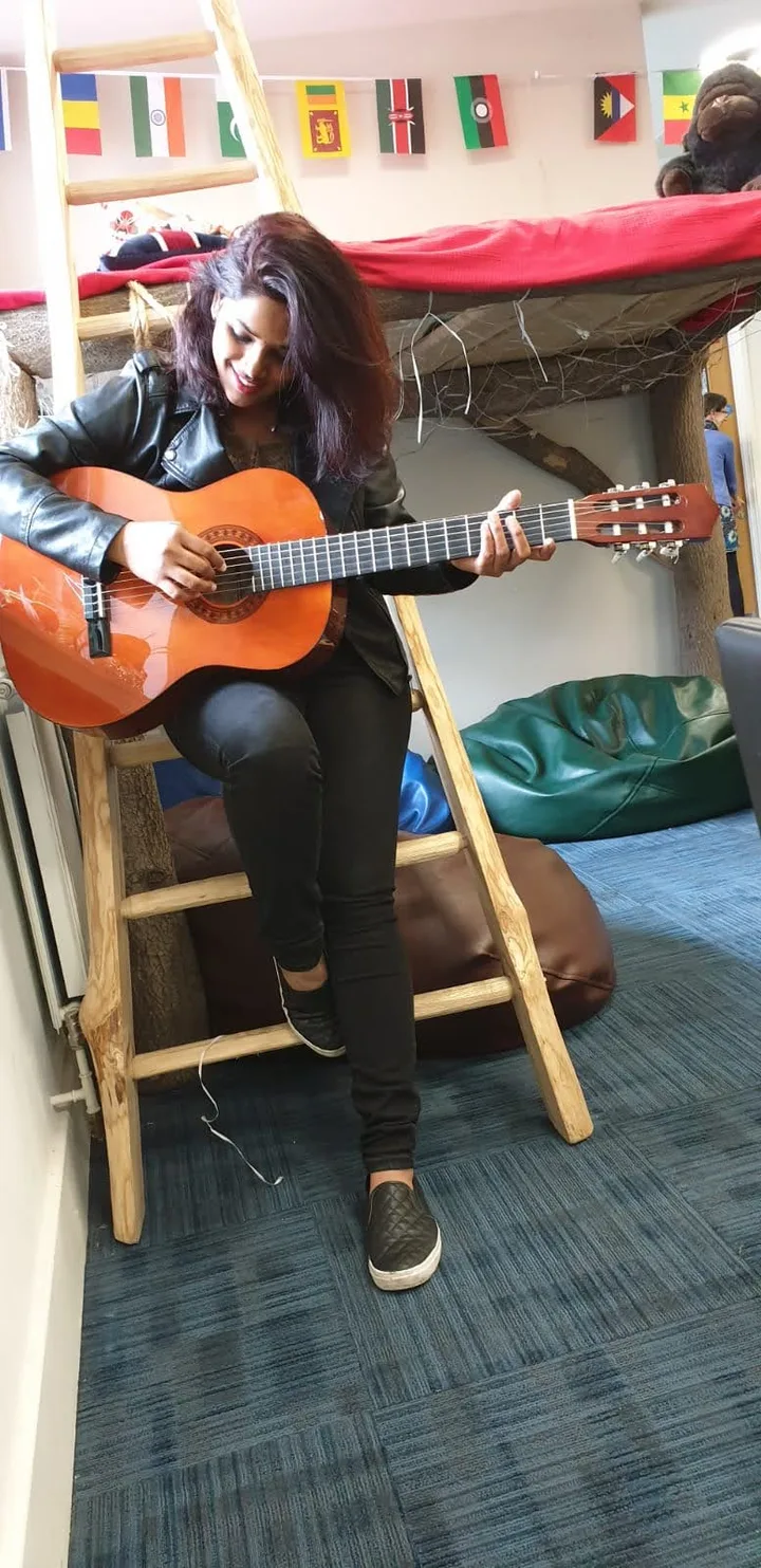 Playing a guitar in a bright room strung with prayer flags.
