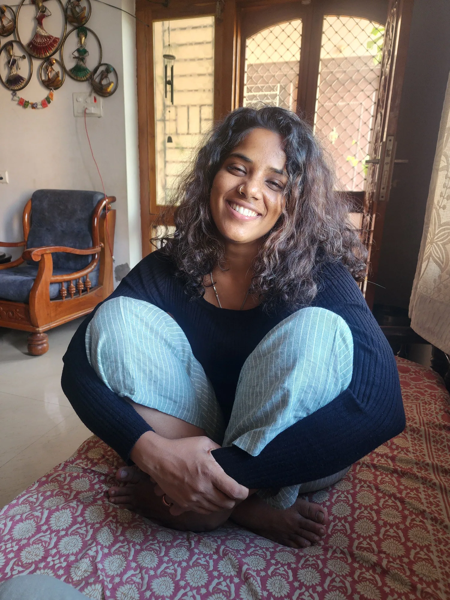 A woman seated by a window in soft light, smiling quietly.