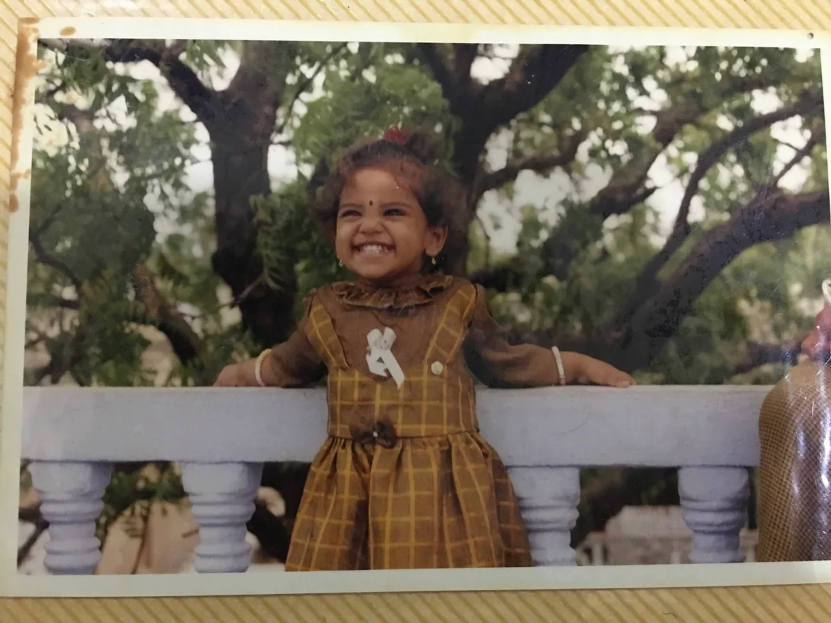 A faded print of a little girl in a brown checked dress, arms flung open along a railing, laughing.