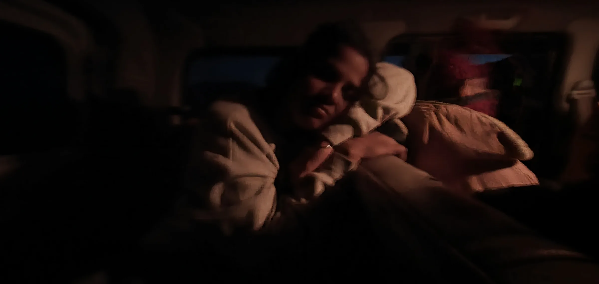 Two friends asleep leaning against each other in a dark vehicle.