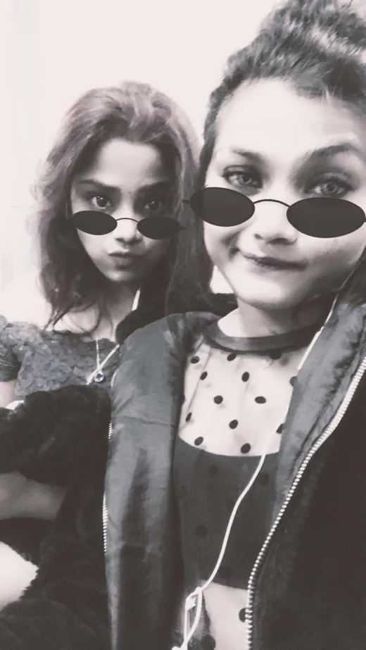 Two friends wearing small round sunglasses, pulling deadpan faces.