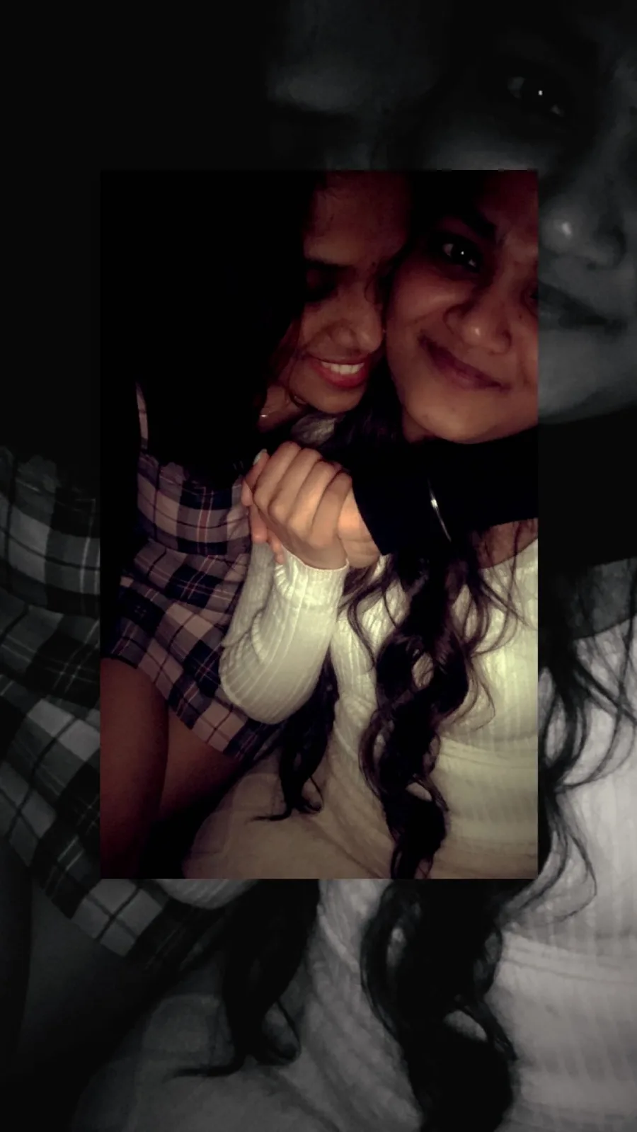 Two friends leaning together, laughing, in a dark room.