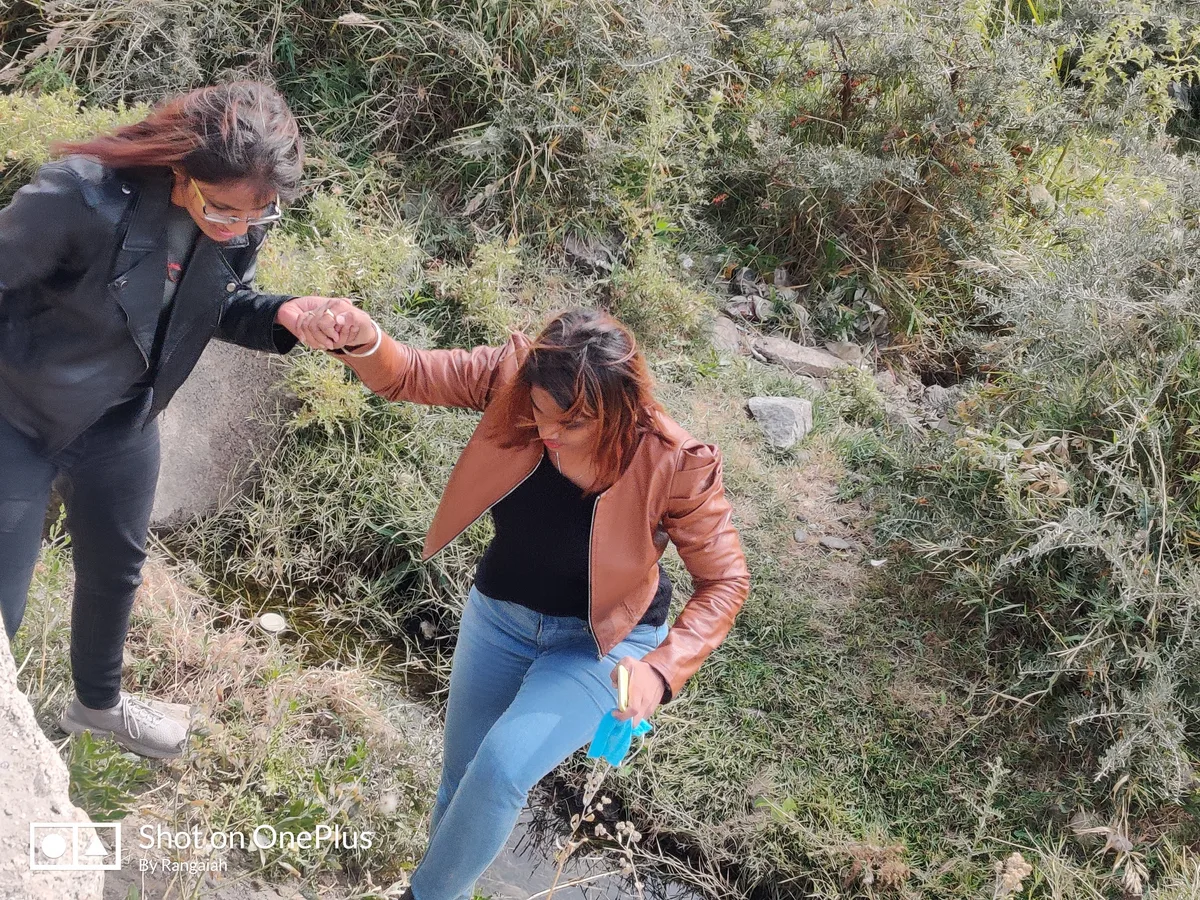 Two women picking their way down a rocky slope, one holding the other by the hand.