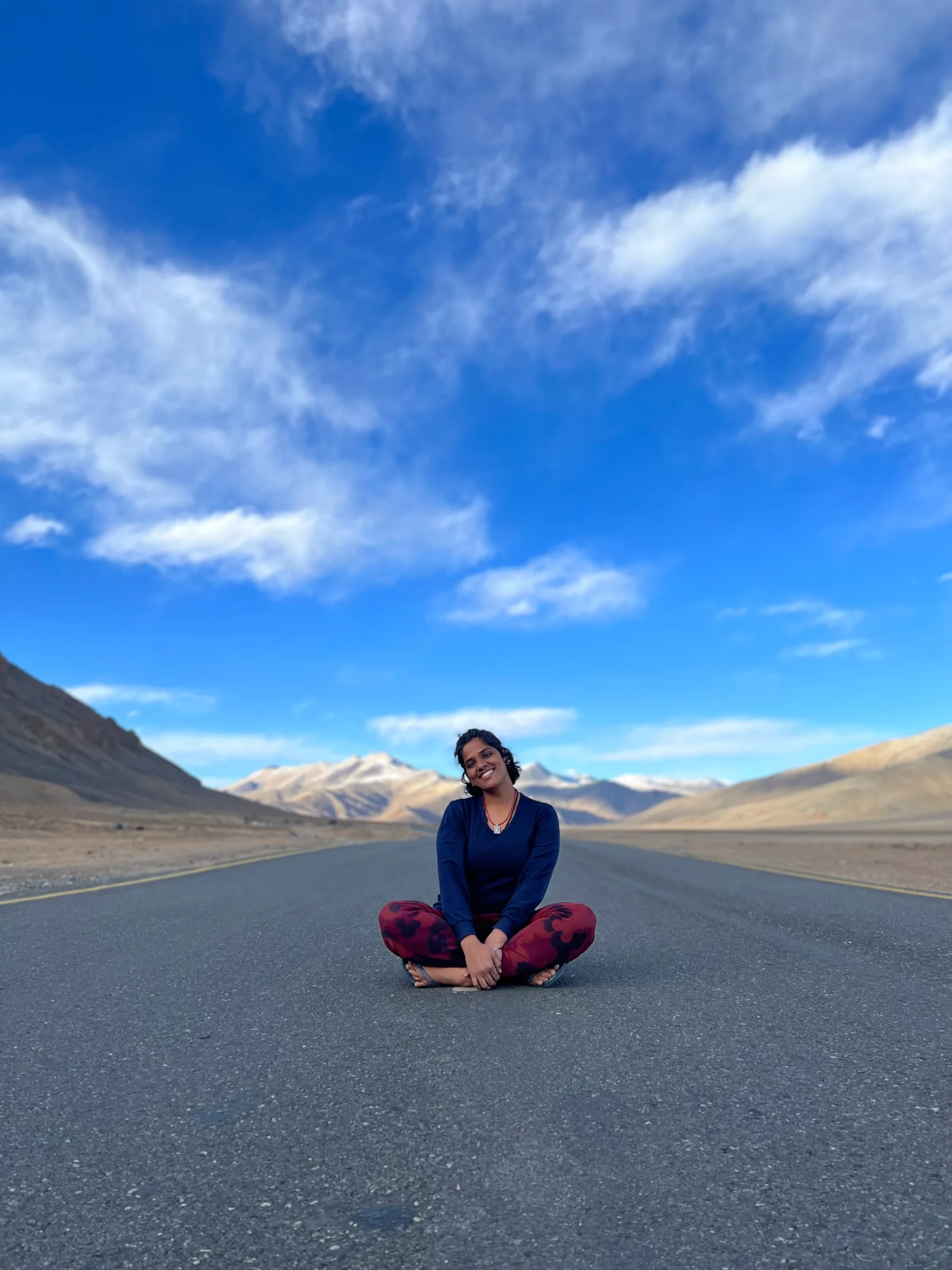 A woman sitting cross-legged in the middle of an empty mountain road.