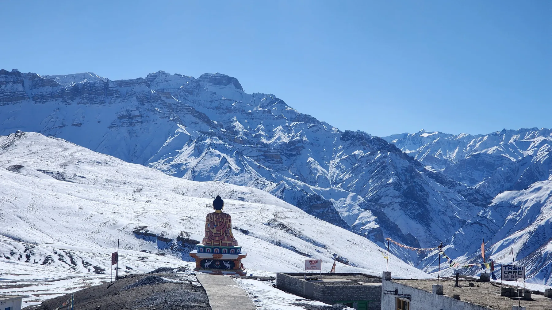 A single seated figure, very small, before an immense range of snow mountains.