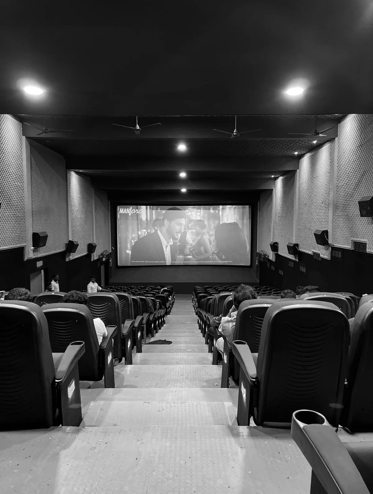 Rows of empty cinema seats facing a lit screen, in black and white.