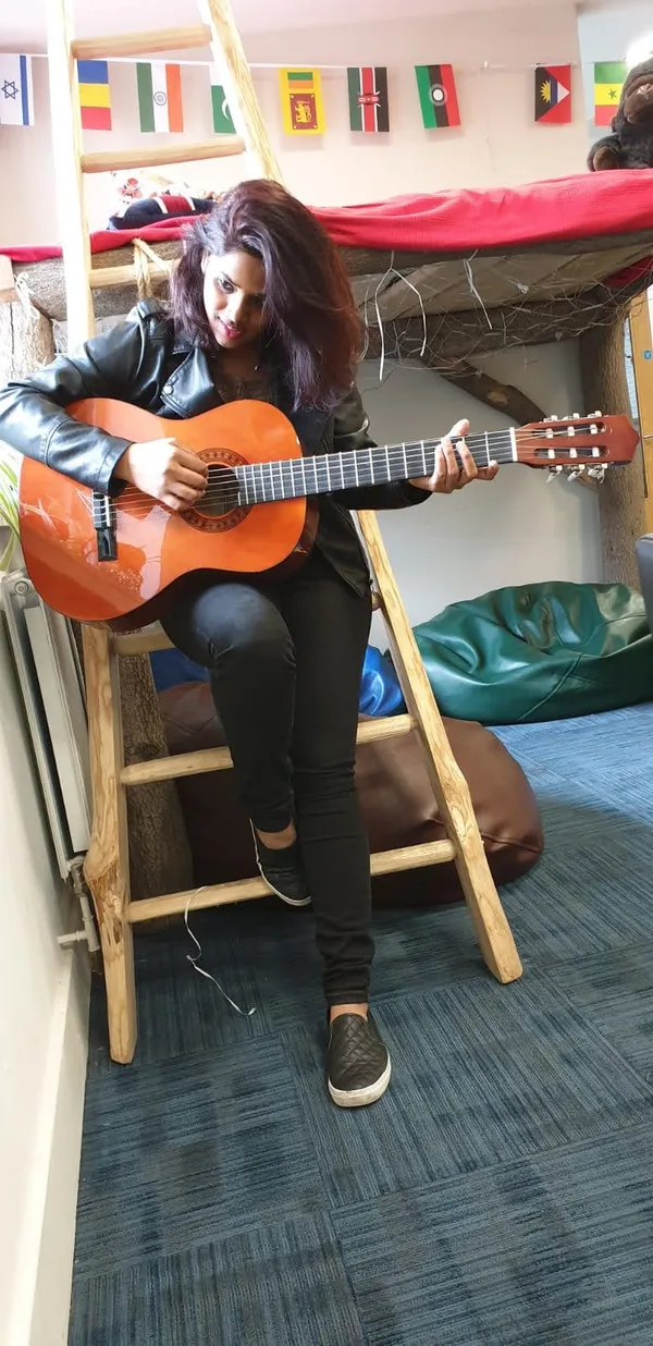 A woman playing an acoustic guitar in a bright room strung with flags.