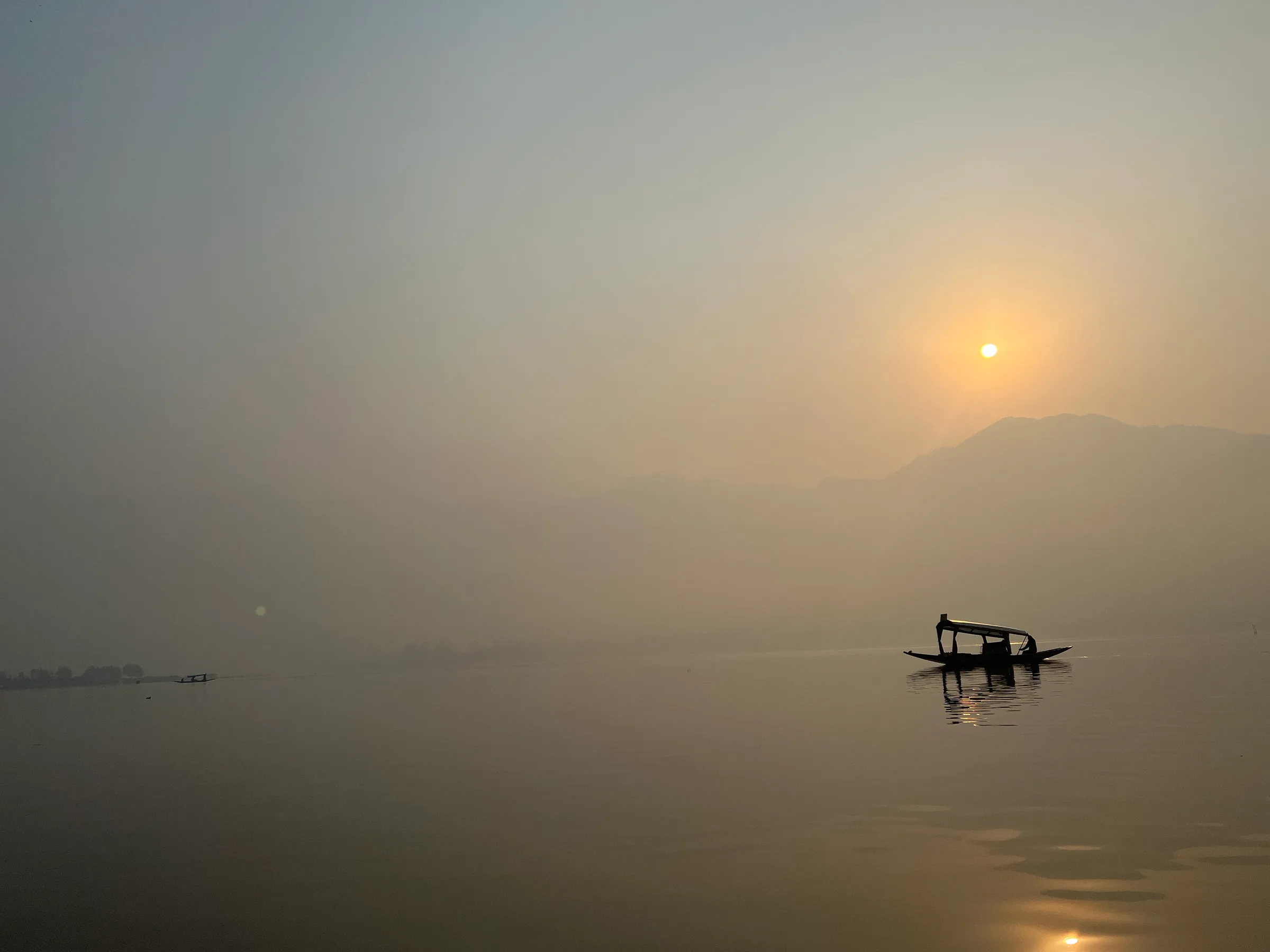 A lone boat on a misty lake at sunrise, the water perfectly still.